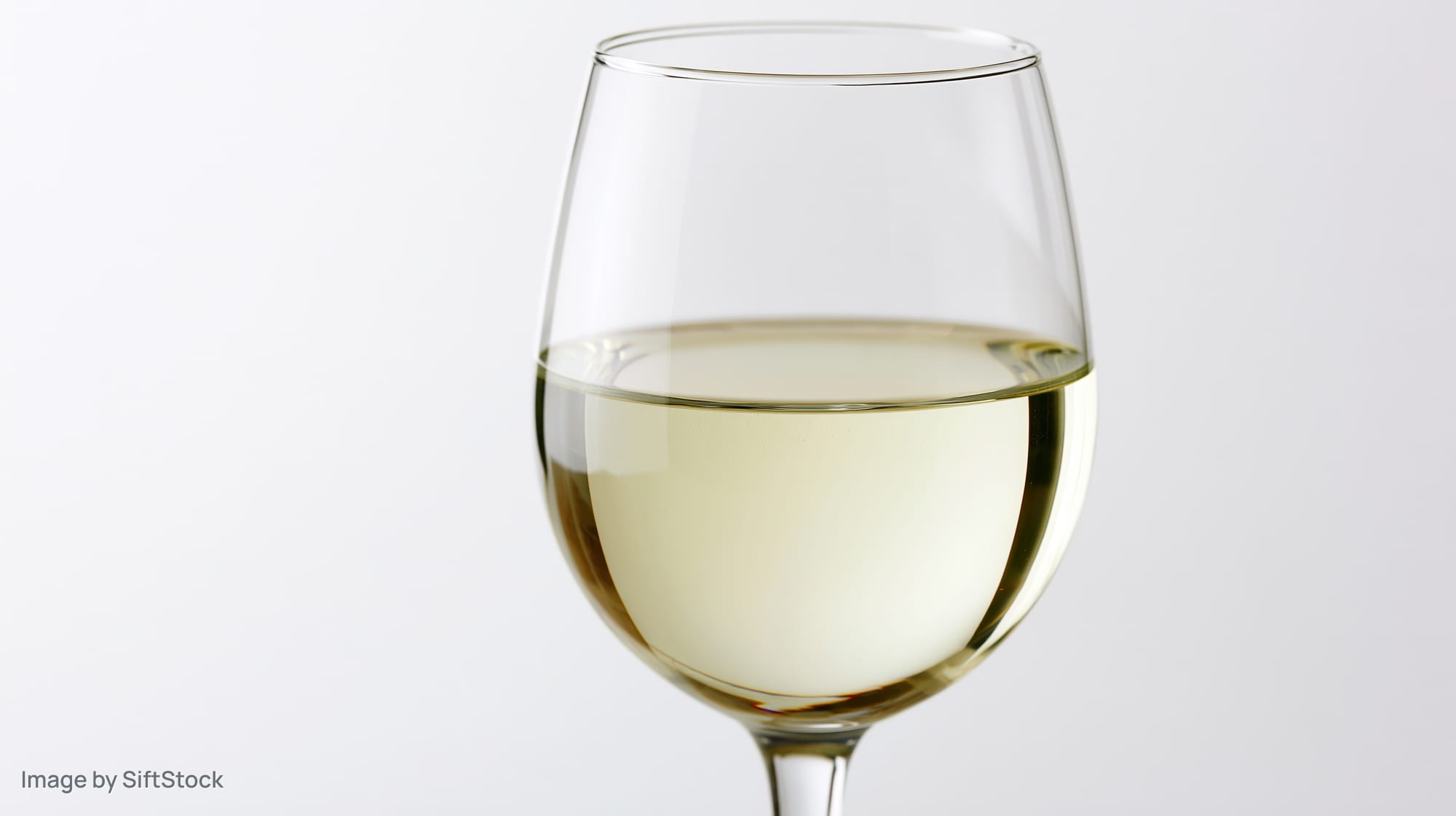 A tulip-shaped wine glass half-filled with pale straw-colored white wine on a white background