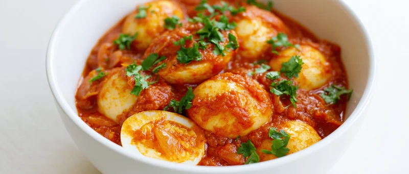 Indian egg curry with halved boiled eggs in tomato sauce served in a white ceramic bowl