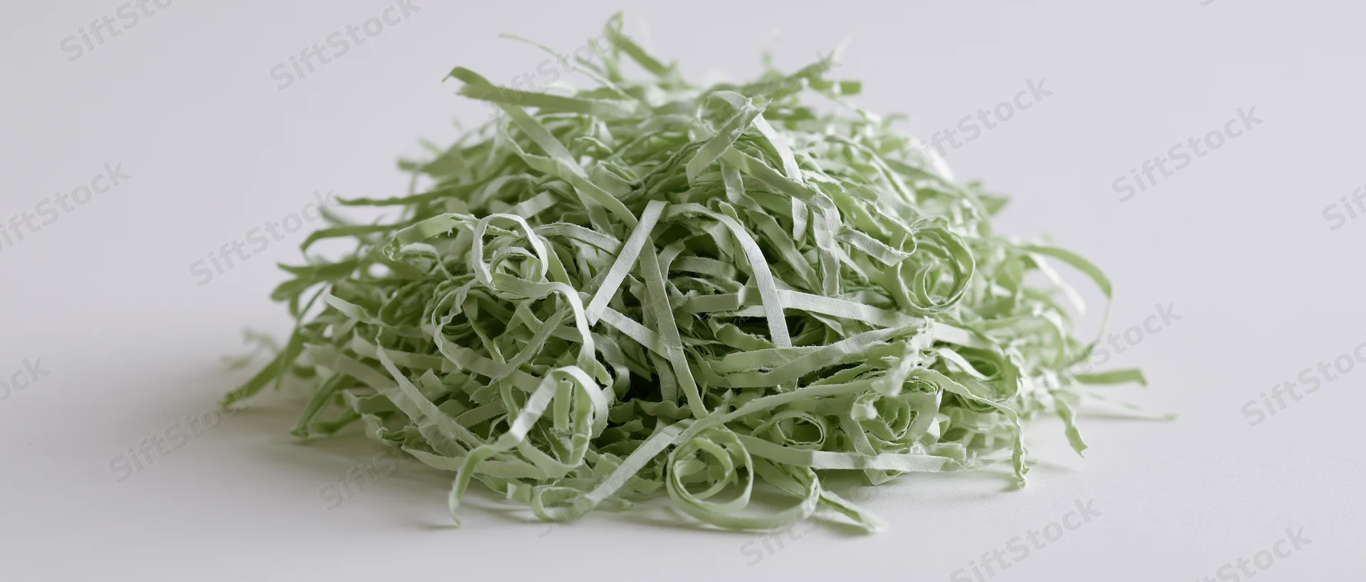 Pile of green shredded paper Easter grass filler on white surface