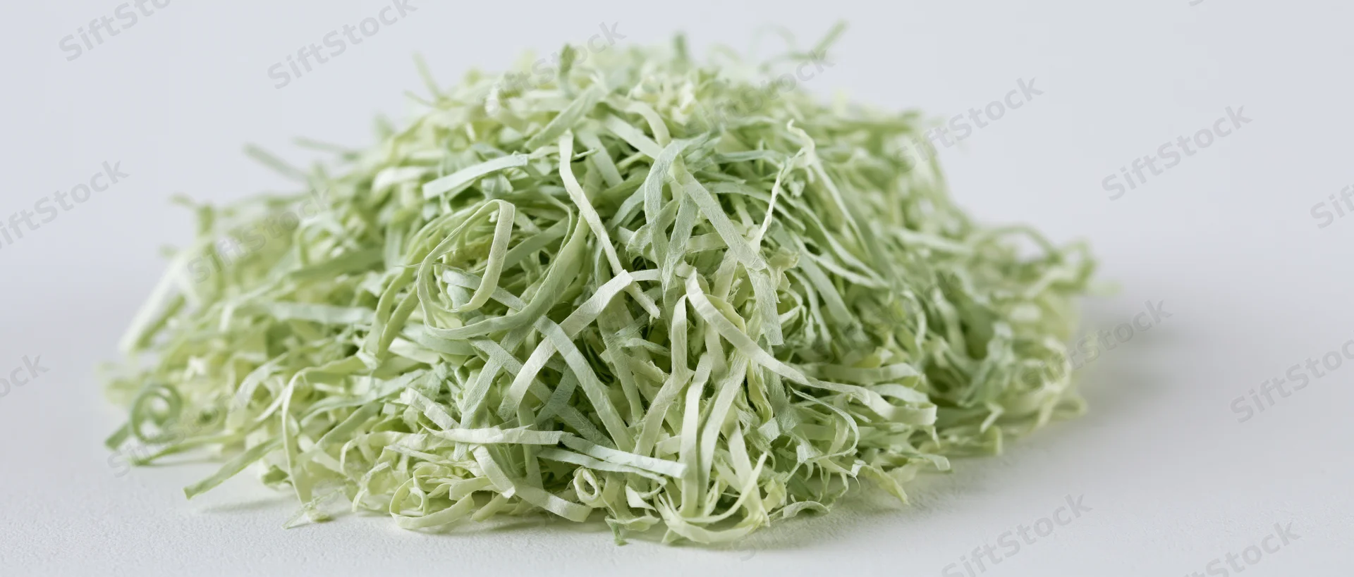 Pile of green shredded paper Easter grass filler on white surface