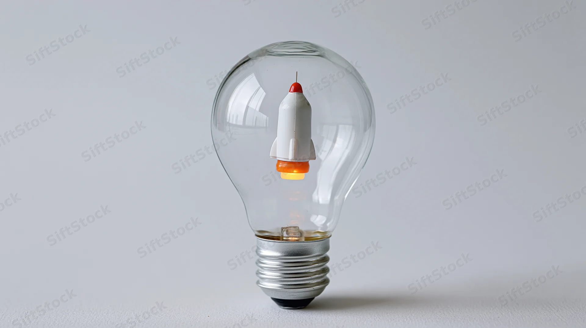 A toy rocket suspended inside a clear lightbulb on a plain surface