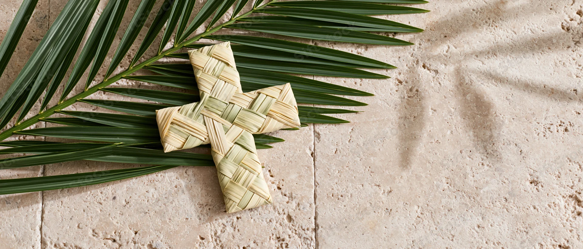 Woven palm frond cross resting on stone tiles with fresh green leaves