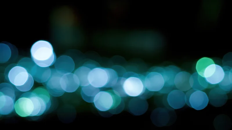 Blurred circular lights in blue and green tones against a dark background