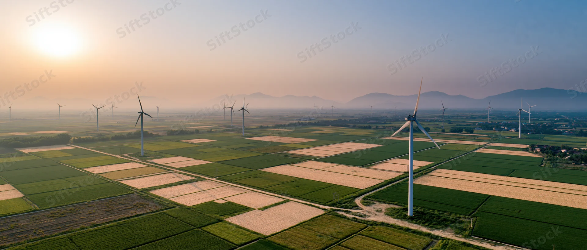 Aerial view of wind turbines scattered across patchwork farmland at sunset