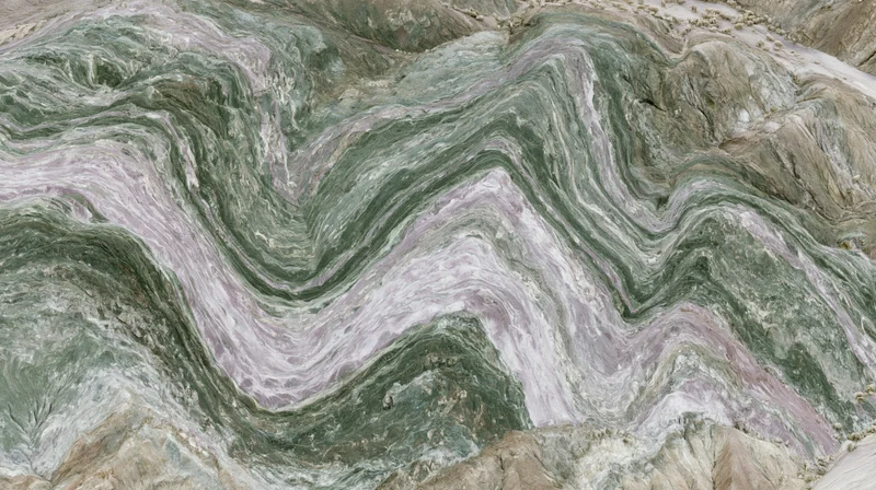 Aerial view of layered sedimentary rock formation with undulating strata and mineral veins