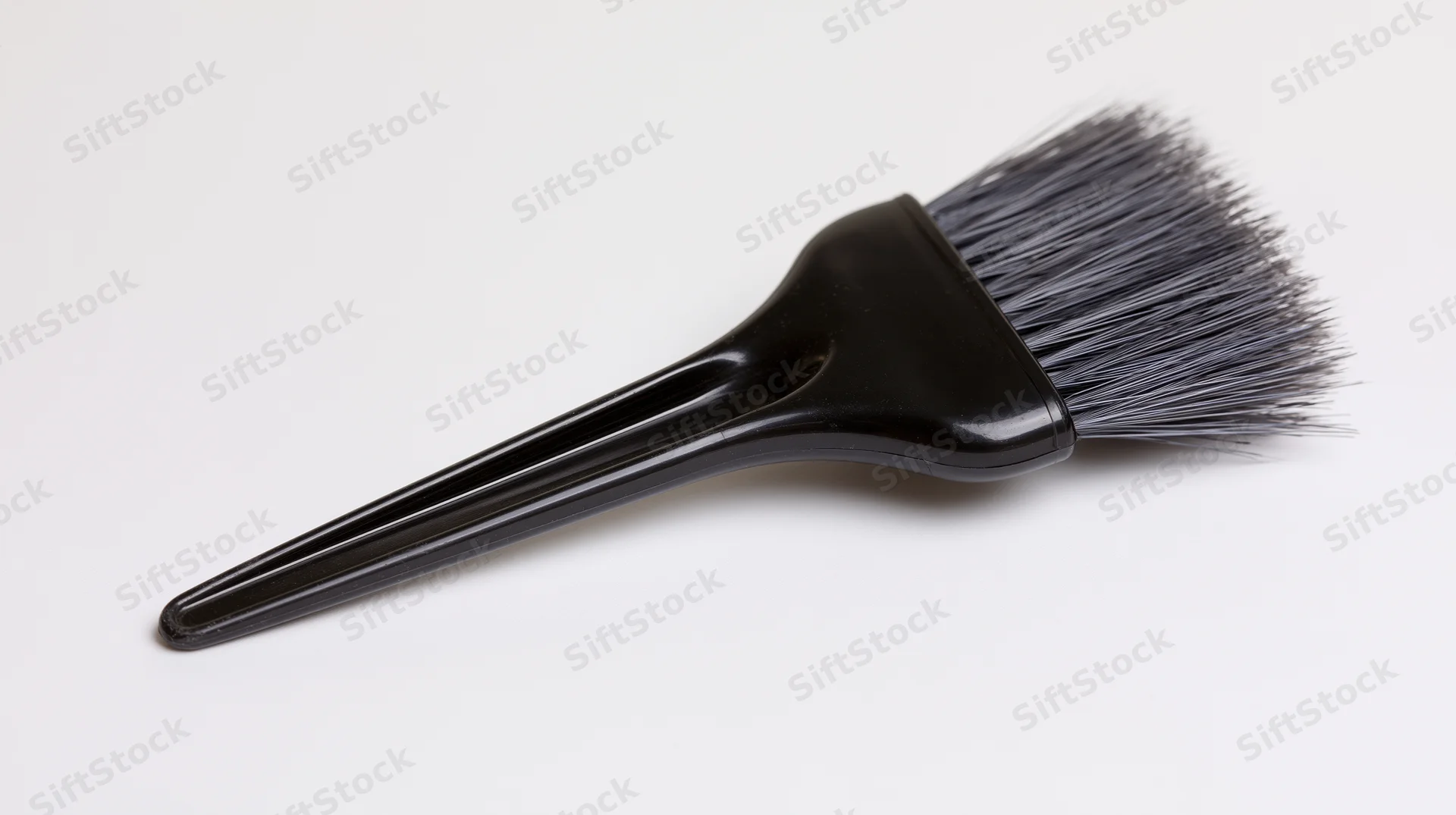 Black plastic hair dye applicator brush with dense grey bristles on white background