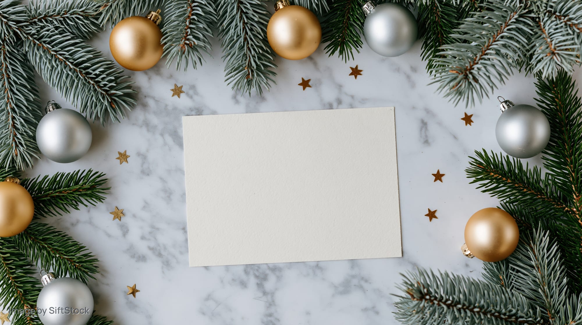 Blank cream card centered on marble surface framed by evergreen branches and metallic ornaments