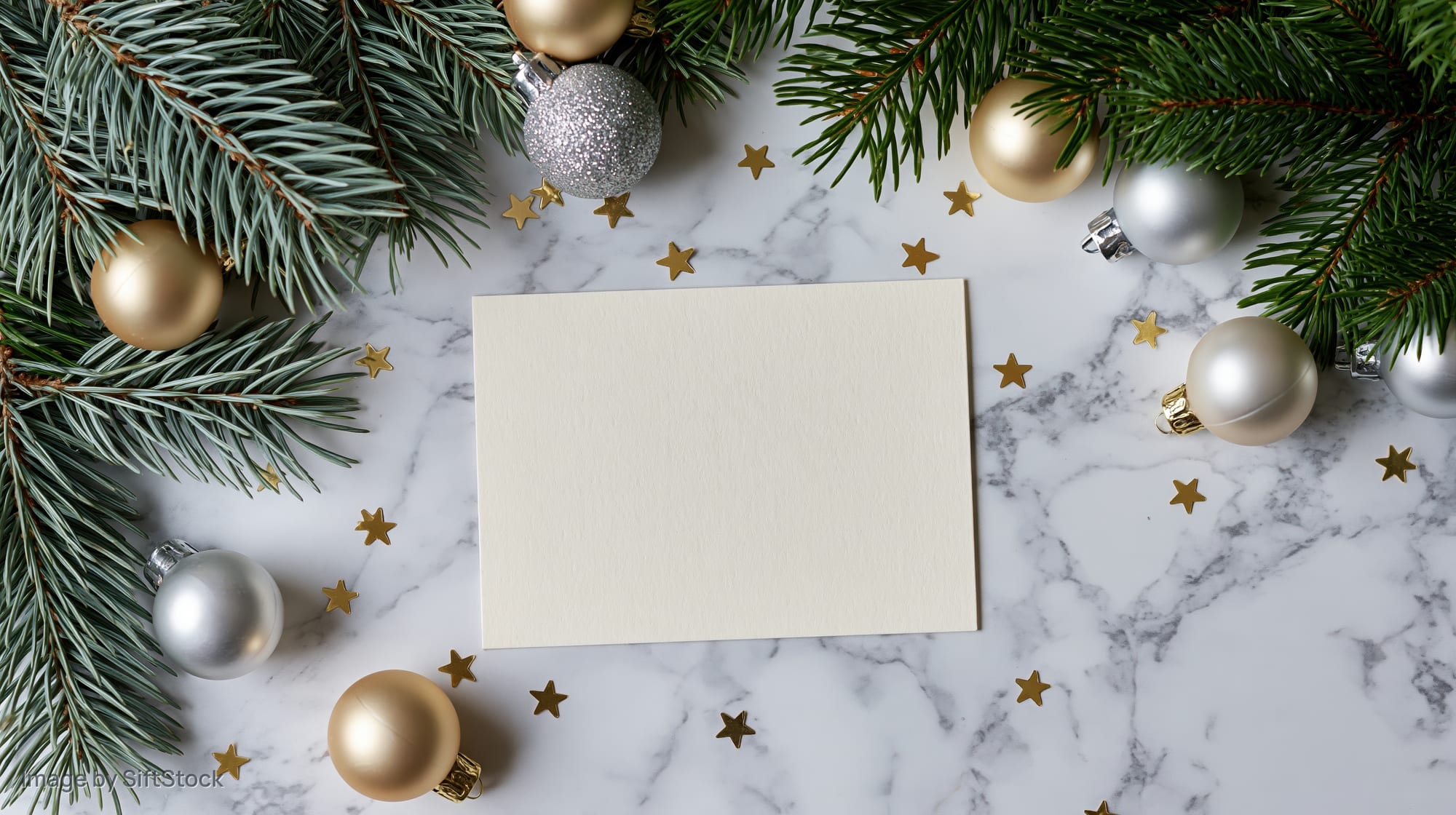 Blank cream card centered on marble surface surrounded by pine branches and ornaments