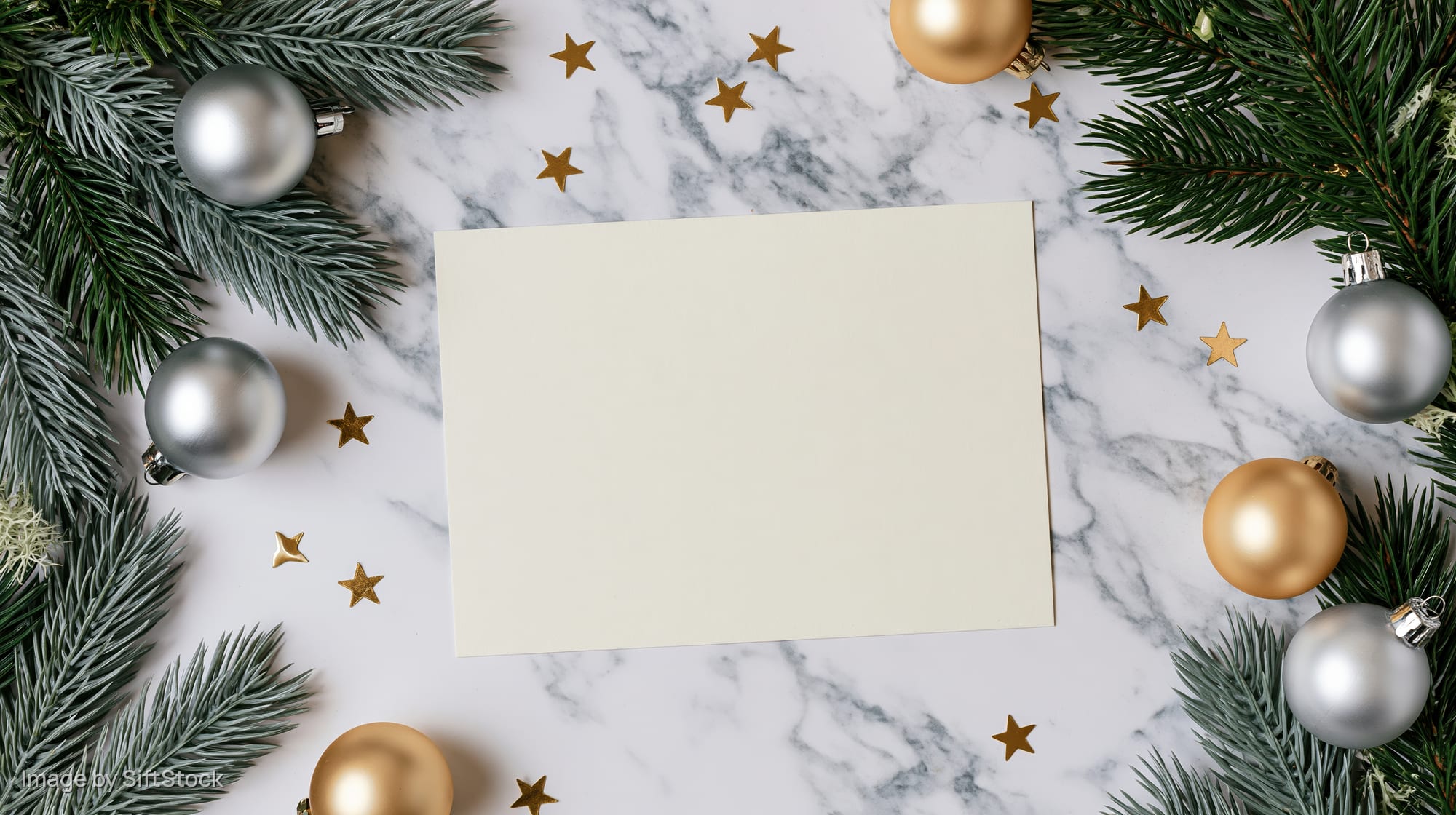 Blank cream card centered on marble surface surrounded by pine branches, gold and silver ornaments, and star decorations for christmas holiday display
