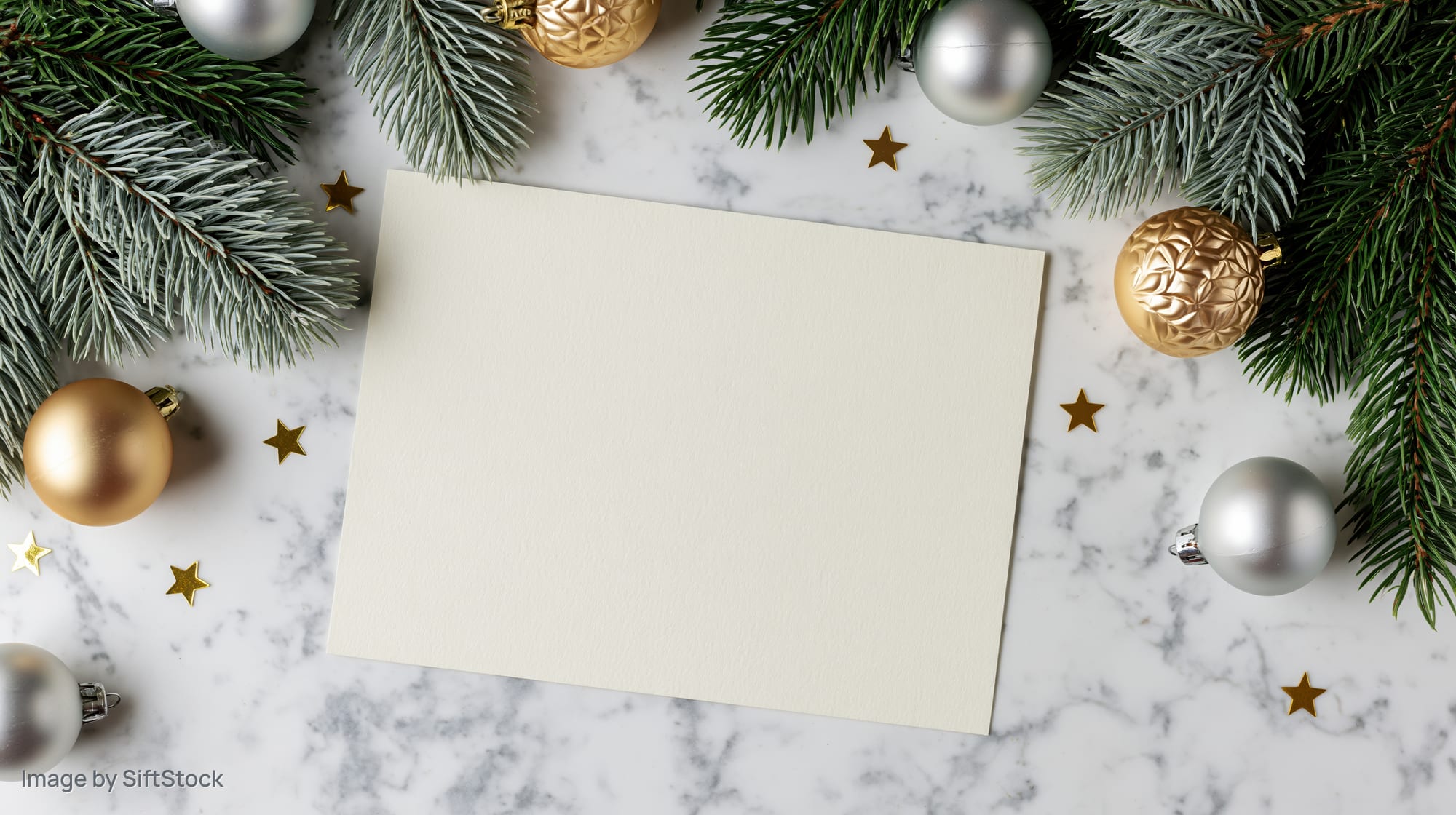 Blank cream card centered on marble surface surrounded by pine branches and ornaments