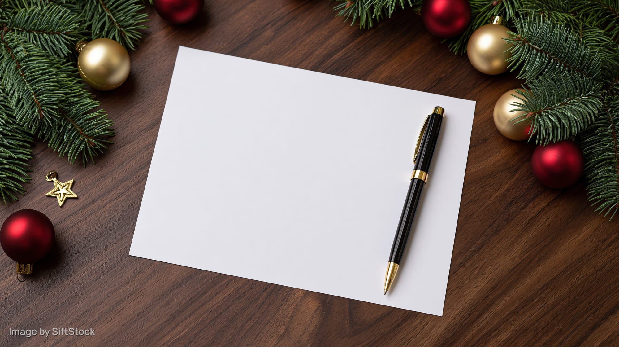 Blank paper with pen on wooden desk surrounded by christmas decorations