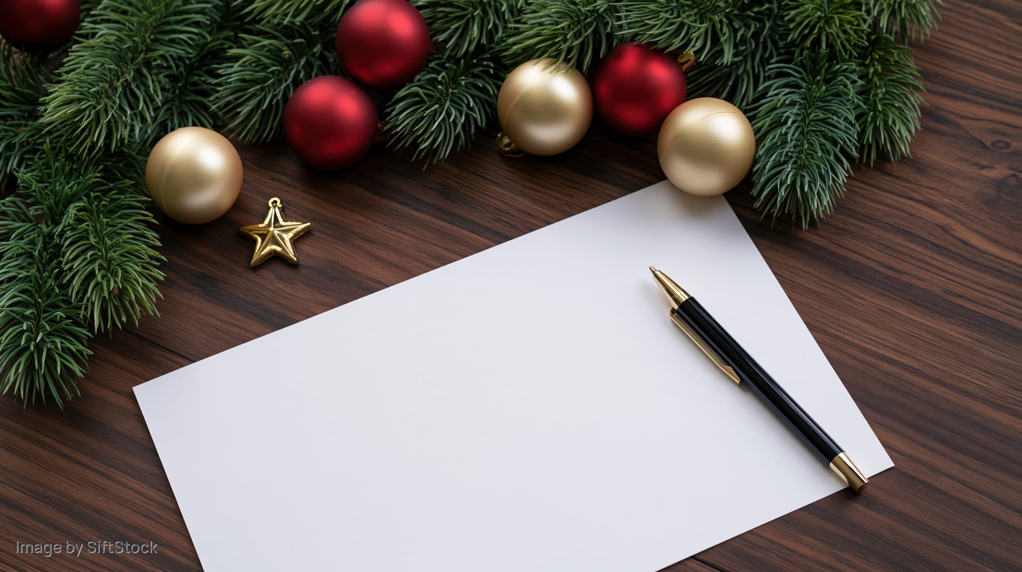 Blank paper with a pen on a wooden desk surrounded by christmas decorations