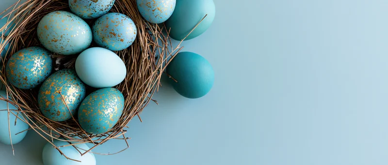 Blue and teal easter eggs with gold speckles in a nest on a light blue surface