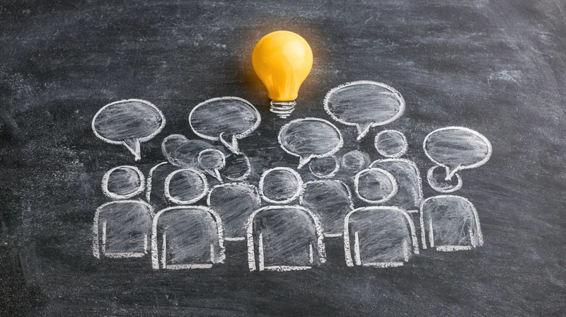 Chalk drawing of a group of people with speech bubbles and a glowing lightbulb on a blackboard