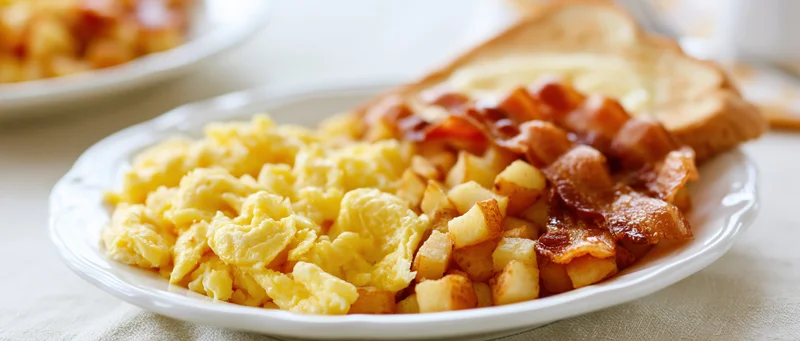 Scrambled eggs with bacon, potatoes and toast on a white plate on a tablecloth