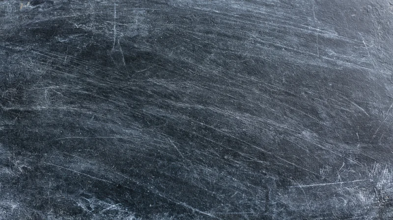 Close-up of a worn blackboard surface with chalk residue and scratches filling the frame