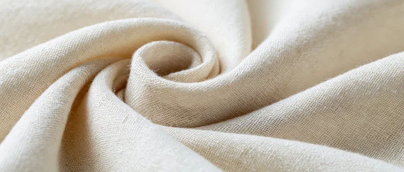 Close-up of natural linen fabric with soft flowing folds and visible weave texture