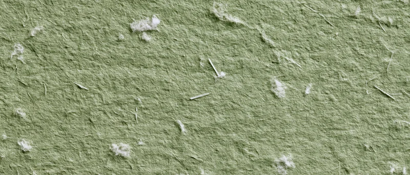 Close-up of sage green handmade paper texture with visible fibers and white flecks