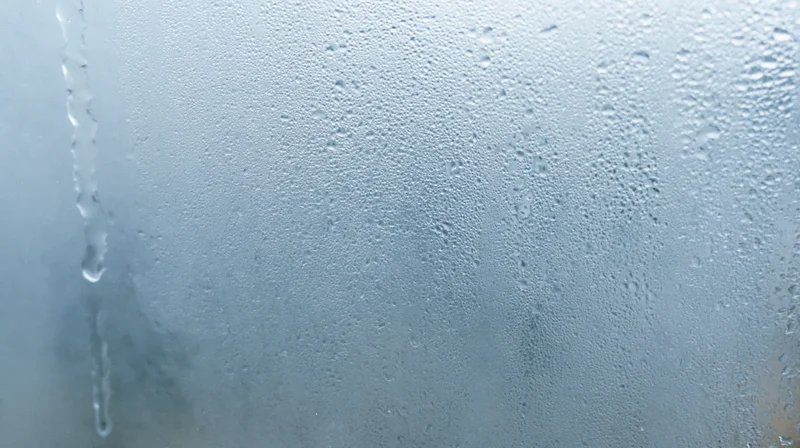 Close-up of fogged window with condensation droplets and steam on glass surface