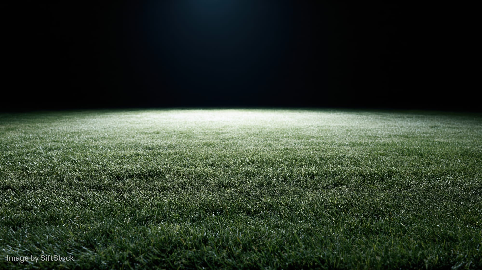 Illuminated grass football pitch at night viewed from ground level
