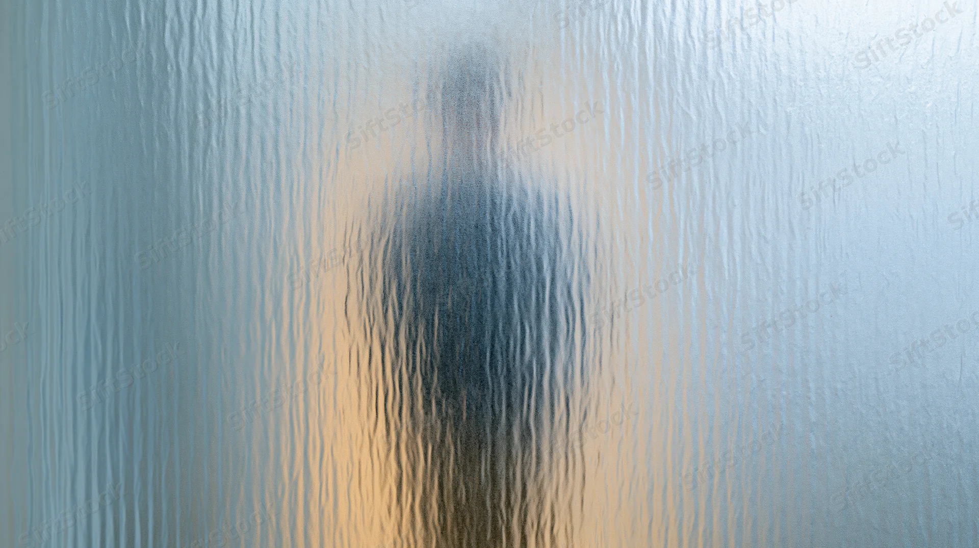 Blurred human silhouette behind textured frosted glass panel in bathroom interior