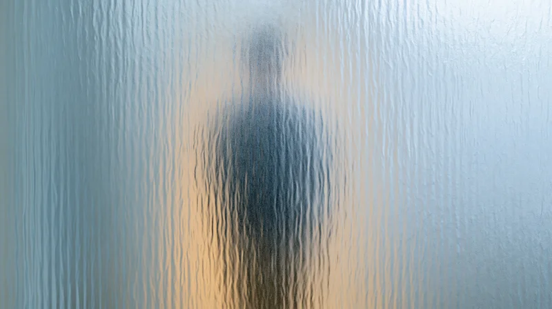 Blurred human silhouette behind textured frosted glass panel in bathroom interior