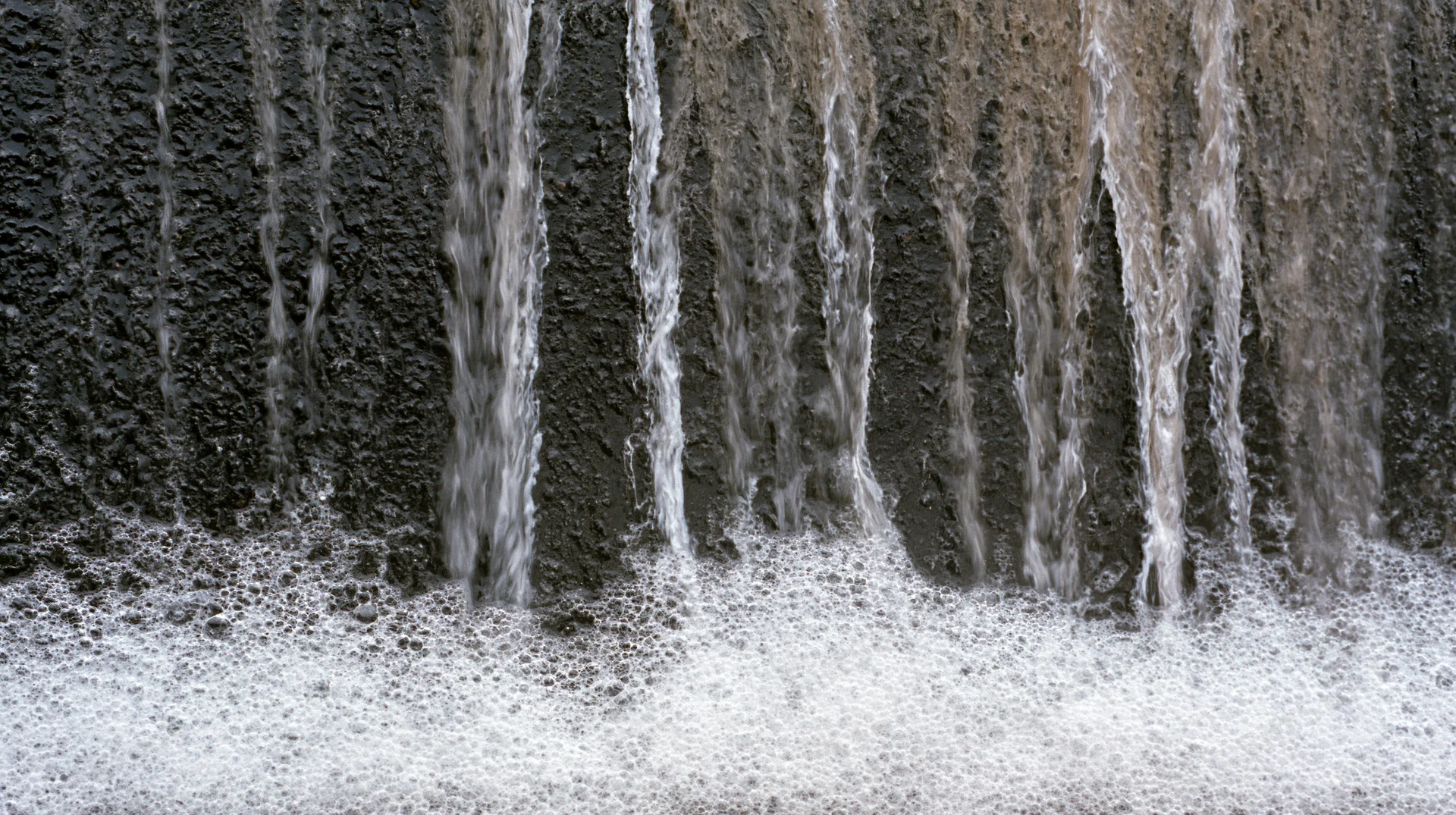 Water streaks and soap foam dripping down a dark textured wall