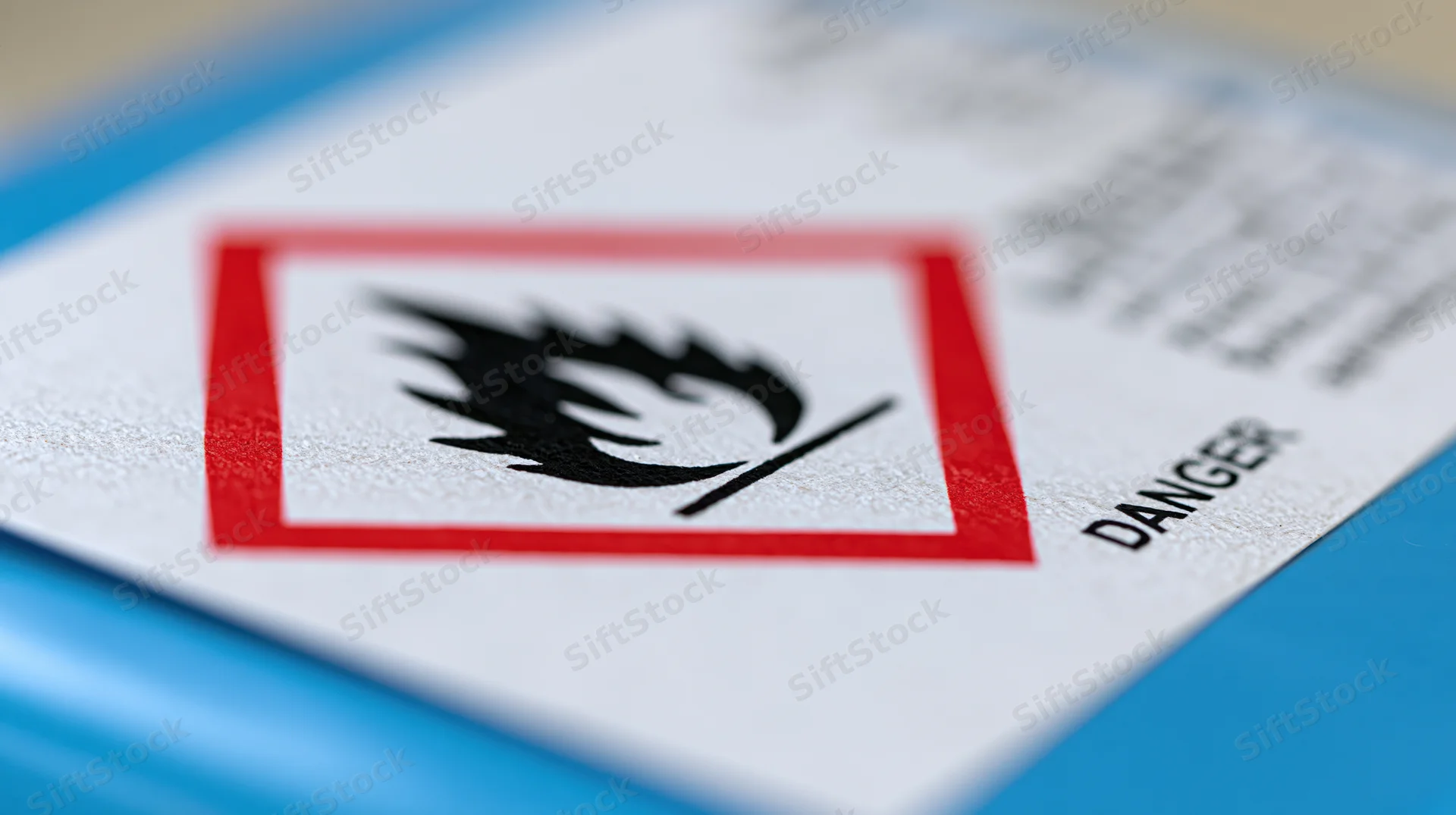 Close-up of a ghs flammable hazard symbol on a white label with red border and danger text