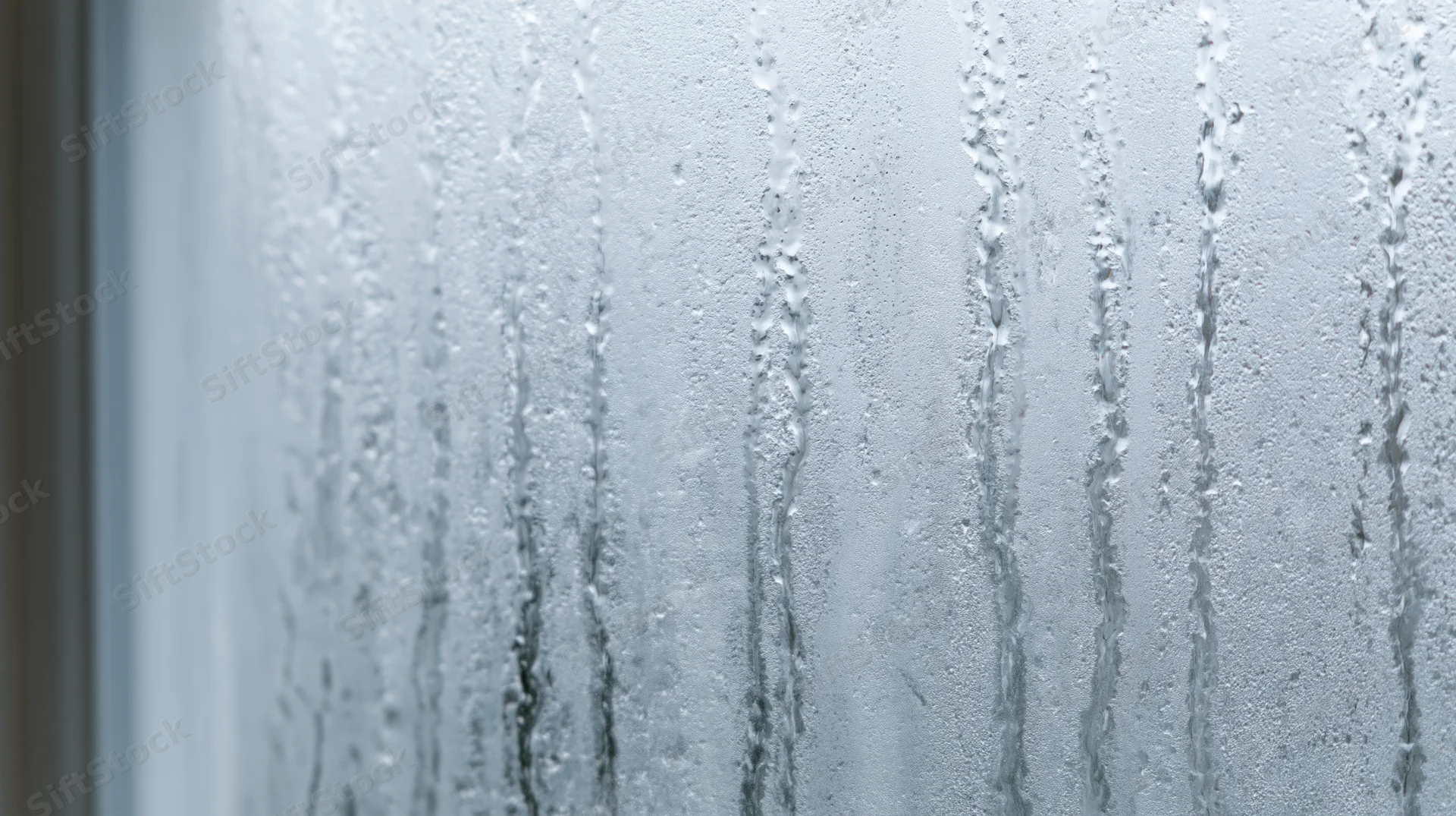 Close-up of condensation droplets streaking down a fogged window pane