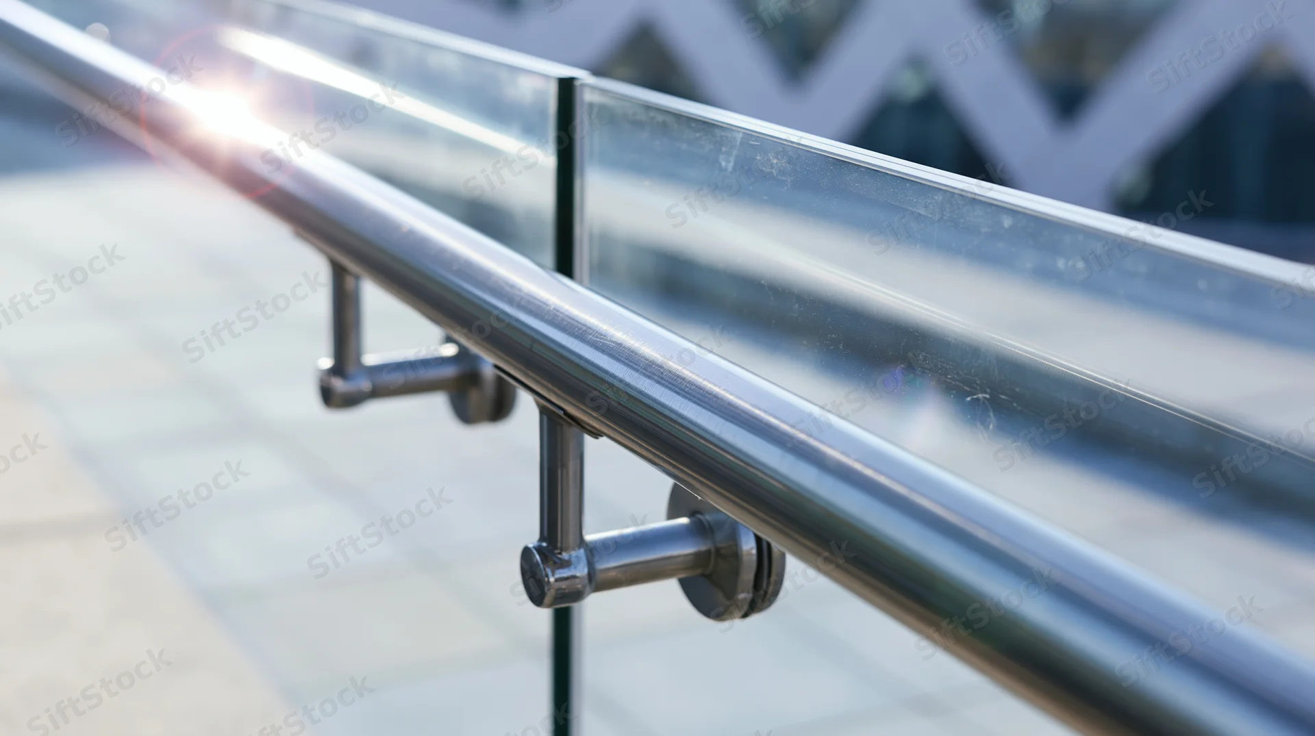 Close-up of a stainless steel handrail with glass panels on an outdoor walkway