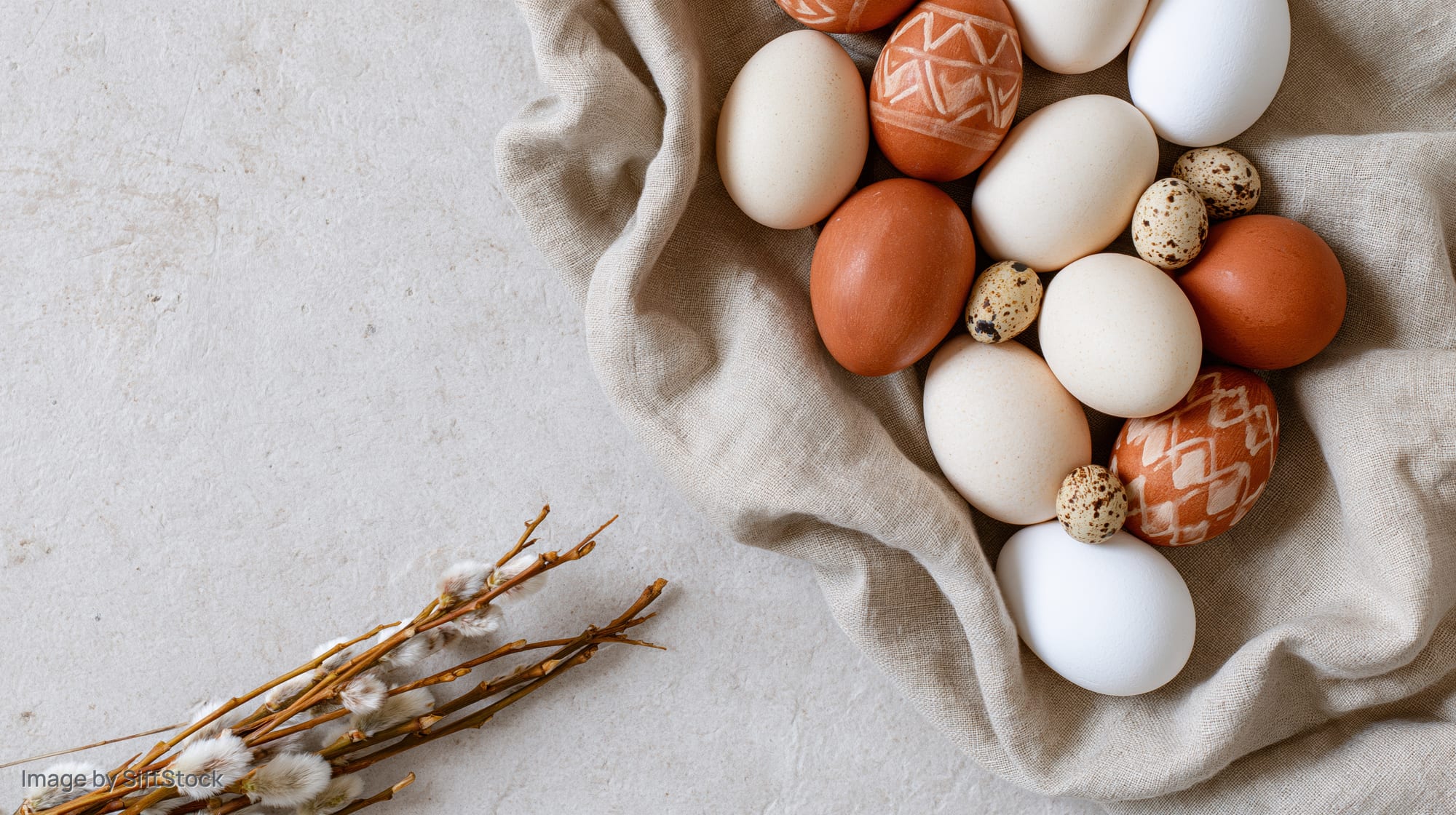 Easter eggs and willow branches arranged on a rumpled linen cloth on a light surface