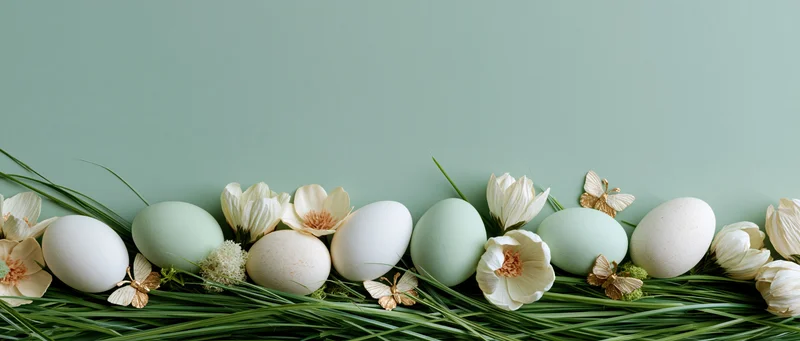 Easter eggs and white flowers arranged on green grass along the bottom edge of a mint background