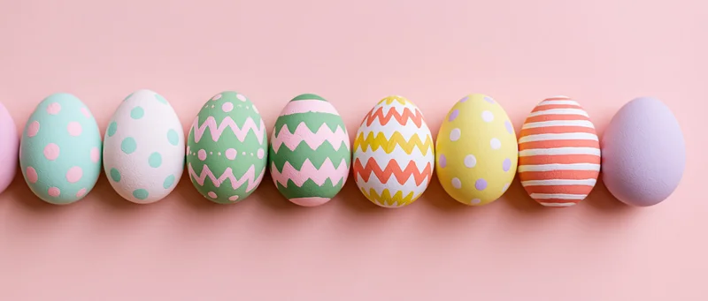 Eight painted easter eggs arranged in a horizontal row on a pink surface