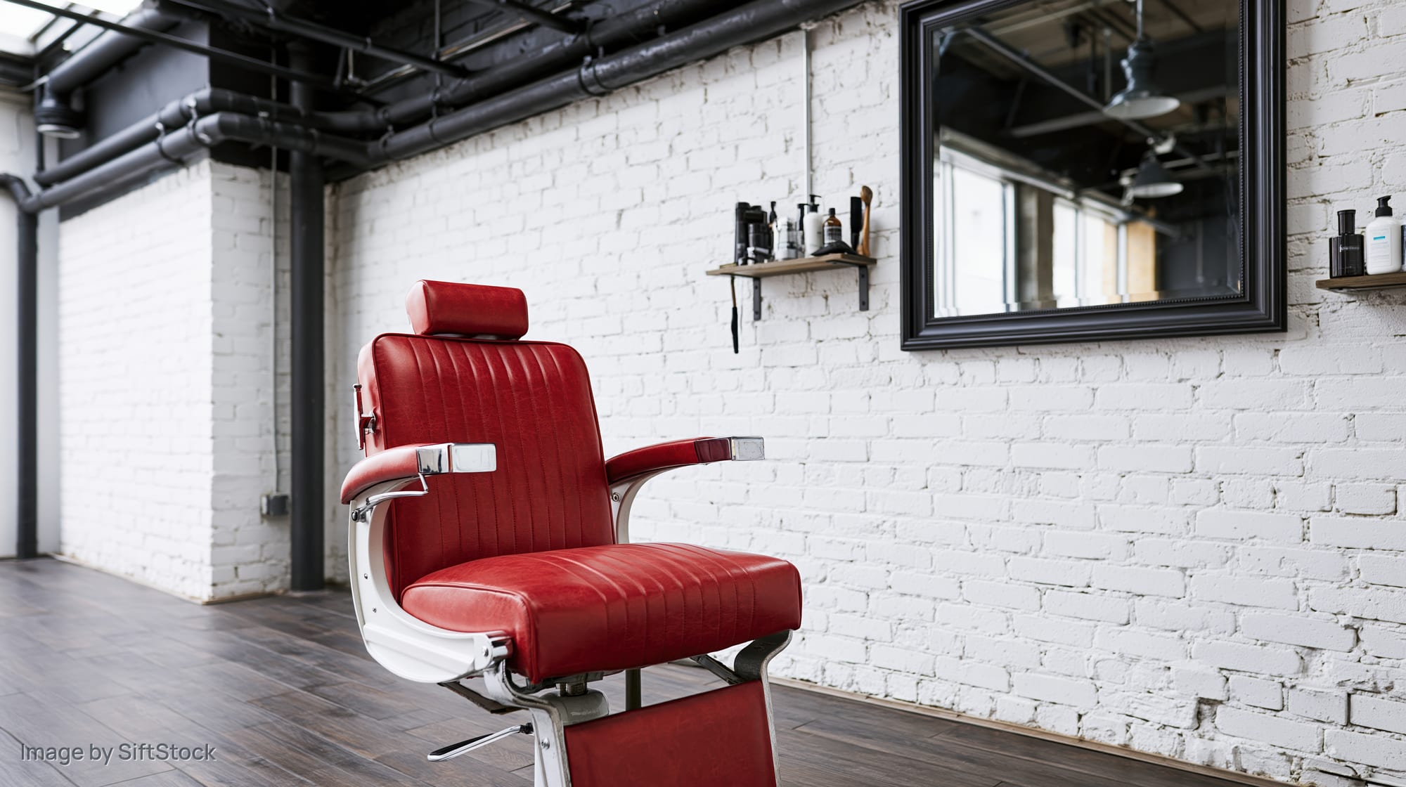 Red vinyl hydraulic barber chair in a modern barbershop interior with white brick walls and industrial ceiling pipes