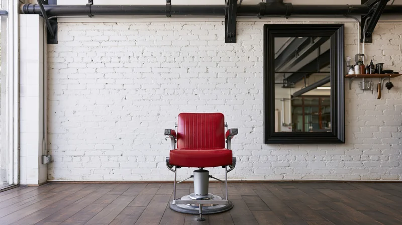 Red vinyl hydraulic styling chair in empty barber shop interior with white brick wall and black mirror