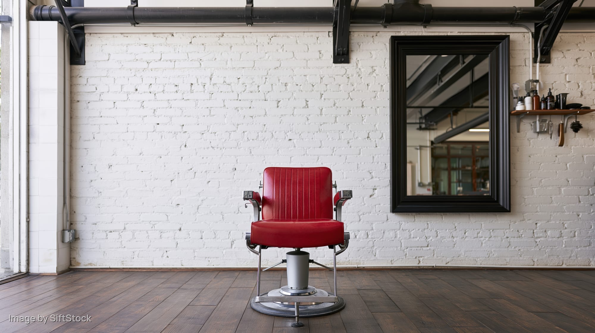 Red vinyl hydraulic styling chair in empty barber shop interior with white brick wall and black mirror
