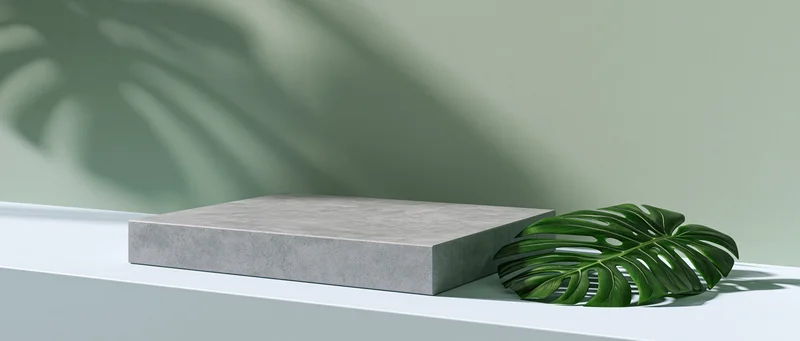 Concrete platform beside a monstera leaf on a white surface with leaf shadows on the wall
