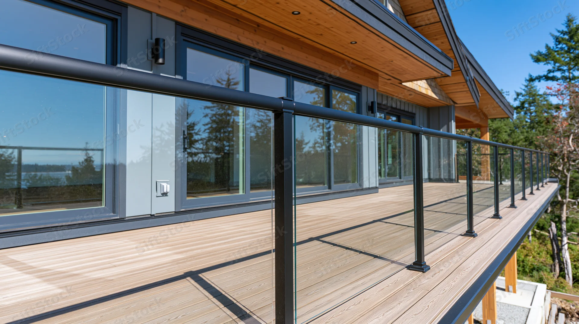 Modern luxury home exterior deck with glass railing and wood flooring overlooking trees and sky