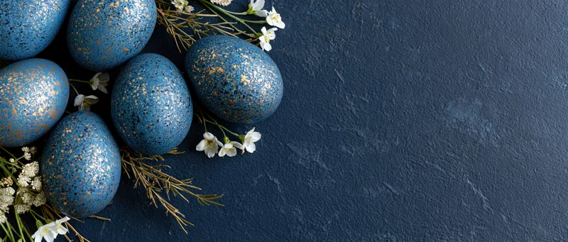 Blue and gold speckled easter eggs arranged with white flowers on dark stone surface