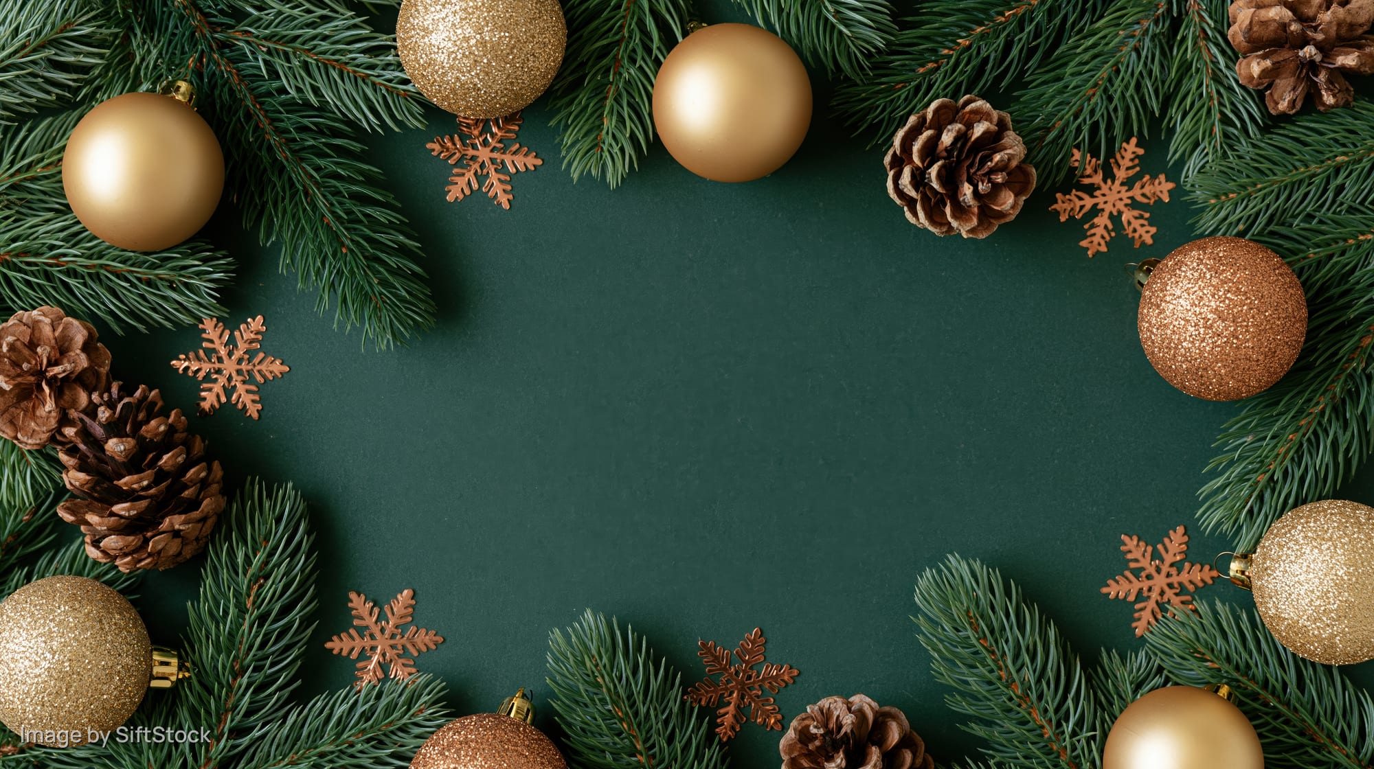 Spruce branches and gold ornaments arranged in a frame on dark green background with copyspace