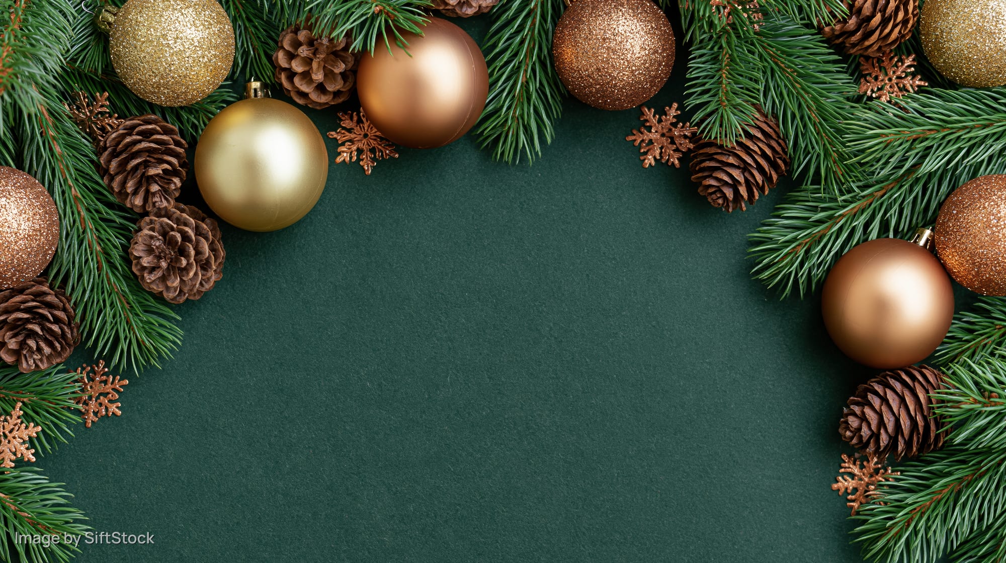 Spruce branches and gold bronze ornaments arranged in a frame on dark green surface with copyspace