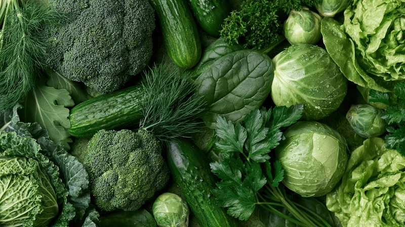 Dense flat lay of mixed green vegetables including broccoli, cucumbers, lettuce, kale, cabbage, and herbs arranged closely together