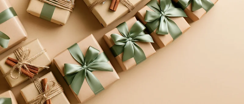 Multiple kraft paper gift boxes with green ribbons and cinnamon sticks arranged in flat lay on beige surface
