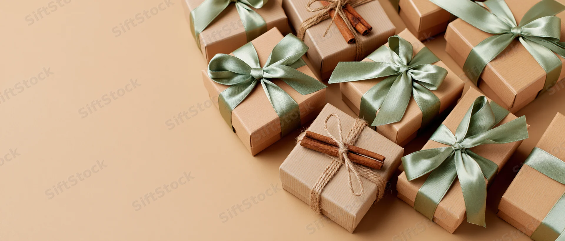 Multiple kraft paper gift boxes with green ribbons and cinnamon sticks arranged in a flat lay on a beige surface