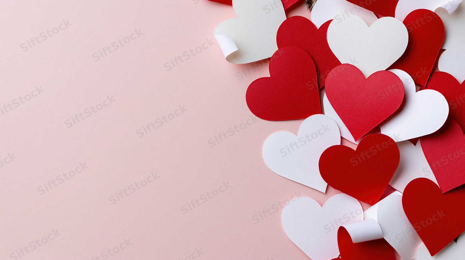 Red and white paper heart cutouts arranged along the right side of a pink surface