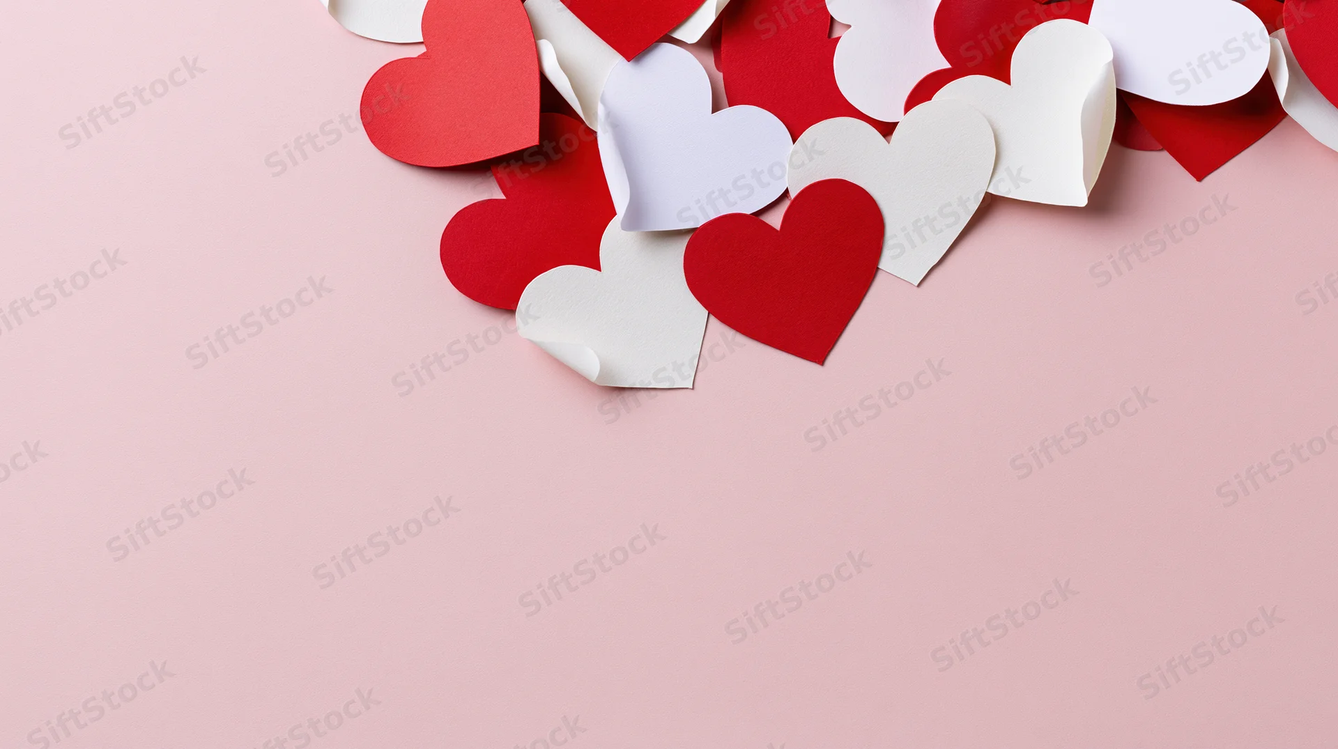 Red and white paper hearts arranged along the top edge of a pink surface with copyspace below