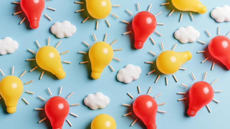 Flat lay of red and yellow plastic lightbulbs with toothpick rays and white clouds on blue background