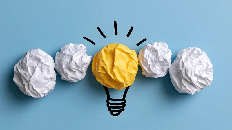 Crumpled paper balls arranged in a row with one yellow ball shaped as a lightbulb on blue background