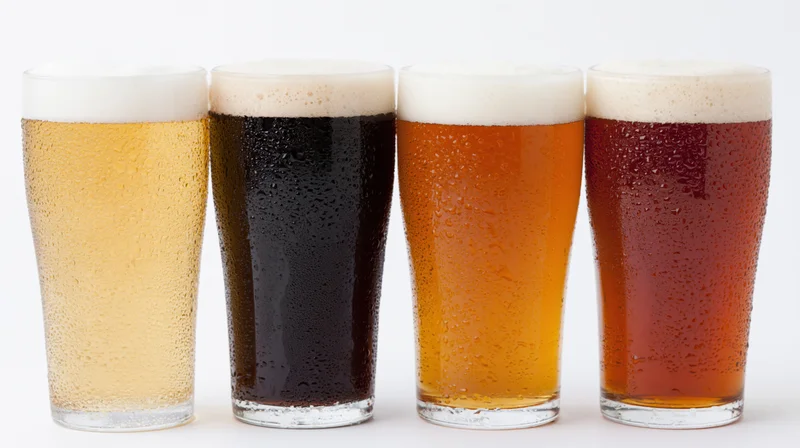 Four pint glasses of different beer varieties lined up in a row on white background