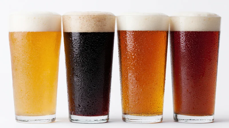 Four pint glasses of different beer varieties lined up in a row on a white background